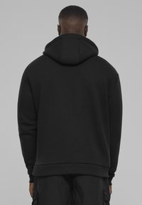 Čierna mikina s kapucňou a voľným strihom, s rebrovaným lemom a manžetami. Hladká textúra s minimálnym detailom.