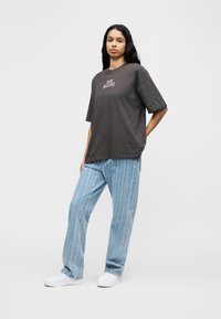 Γκρι βαμβακερό t-shirt με το λ ογότυπο "NEW BALANCE", συνδυασμένο με ανοιχτόχρωμα τζιν με ρίγες και λευκά αθλητικά παπούτσια. Άνετη εφαρμογή.