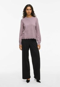 Pull en tricot violet clair avec un col et un ourlet en bordure festonnée. Assorti à un pantalon large noir et des escarpins noirs pointus.