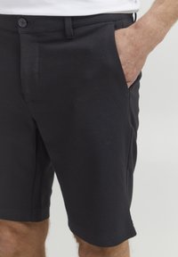 Shorts noirs en stretch fabriqués dans un tissu léger, avec une fermeture à bouton, des poches latérales et une coupe ajustée, arrivant au-dessus du genou.
