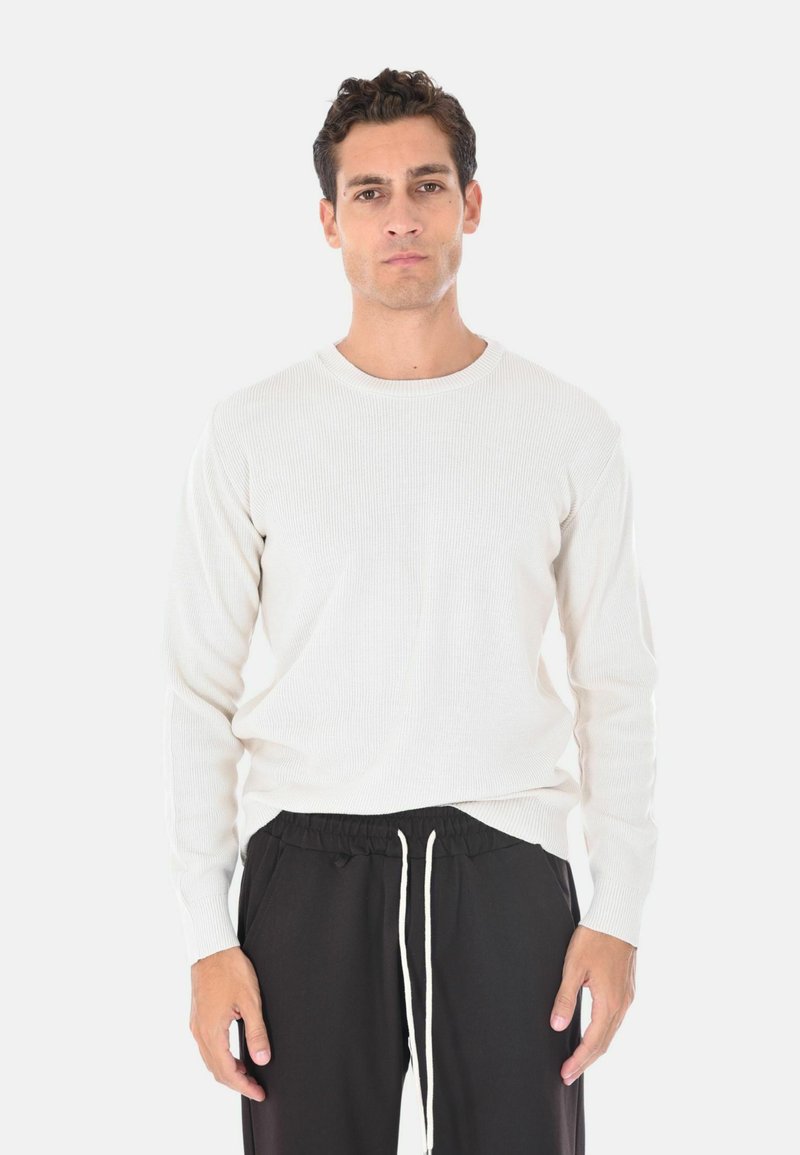 Maglione a maniche lunghe con collo girocollo a costine in beige chiaro, realizzato in tessuto a maglia. Abbinato a pantaloni neri con cordoncino caratterizzati da una vestibilità comoda.
