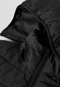 Dettaglio ravvicinato di una giacca nera imbottita con zip e cappuccio, che mostra la texture del tessuto e i dettagli delle cuciture.
