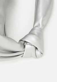 Srebrny supeł z imitacji skóry, charakteryzujący się gładką fakturą i delikatnym połyskiem. Projekt podkreśla rzeźbiarski, minimalistyczny kształt.