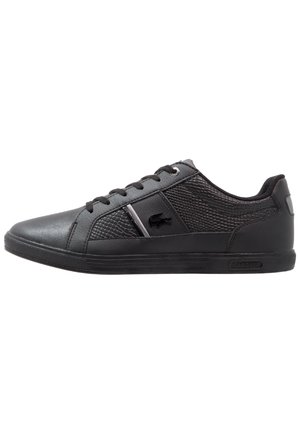 Baskets basses noires avec des panneaux latéraux texturés, fermeture à lacets et petit logo crocodile sur le côté.
