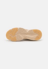 Suola di scarpa sportiva beige con battistrada in gomma tessurizzata, caratterizzata da motivi geometrici e con inserti in gomma arancione sul tallone e sulla punta.