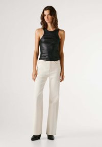 Μαύρο τοπ με λαιμόκοψη halter και λαμπερή υφή, συνδυασμένο με κρεμ παντελόνι ψηλόμεσο και φαρδύ και μαύρες μποτάκια με τακούνι στο αστράγαλο.