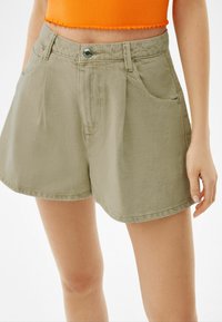 Khakifärgade denimshorts med avslappnad passform. Funktioner inkluderar en framknappstängning, två sidofickor och en ren fåll.