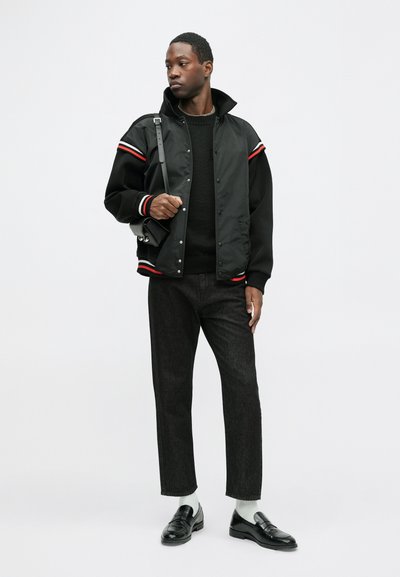 Must musternakk must hapnikrakand juba musta ja valge triibuga, kantud musta sviitri peal, koos tumedate teksade ja mustade mokassiinidega, kandes õlakotti.