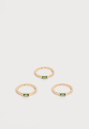 Tres anillos finos de oro con pequeñas piedras preciosas verdes rectangulares, dispuestos sobre un fondo claro y sencillo.