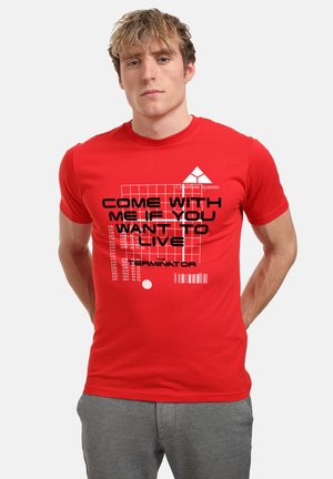 Rød t-shirt med fed sort tekst og grafiske designelementer, herunder "Cyberdyne Systems" og stregkode detaljer. Korte ærmer, rund hals.