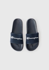 Mornarske plave papuče sa teksturiranim mrežastim trakama na kojima se nalazi bijeli natpis "Champion". Glatka plastična unutrašnjost, otvoreni dizajn za prste.