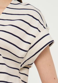 Λευκό κοντομάνικο πουκάμισο με ναυτικό οριζόντιο ρίγες, που φοριέται από άτομο, με το μανίκι σηκωμένο πάνω από τον αγκώνα.