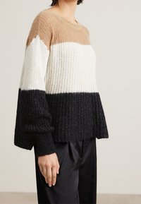 Pull en tricot épais avec un design en blocs de trois couleurs : marron, blanc et noir. Texture côtelée avec de larges manches et un col rond.