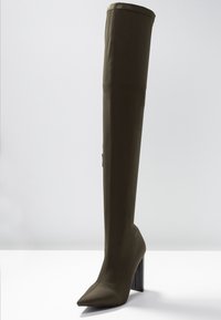 Bota verde oliva por encima de la rodilla hecha de tejido suave, con punta afilada y un tacón negro grueso con un diseño sin costuras.