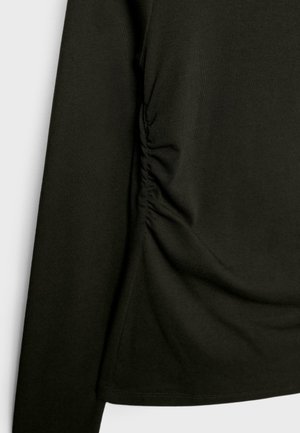 Haut à manches longues noir en tissu lisse et élégant, avec des détails froncés sur le côté, créant un contraste de texture et de forme.