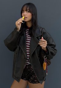 Svart läderoversizedjacka över en bourgogne- och vitrandig skjorta. Glänsande svarta paljettshorts och en brun väska med nyckelring.