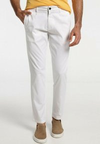 Pantalons blancs ajustés en tissu léger, avec une coupe droite, des poches latérales et une fermeture à bouton. Assortis à des chaussures à enfiler beiges.
