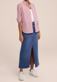 Red and white striped button-up shirt layered over a white tank top, paired with a long blue denim skirt featuring a front slit and white sneakers.