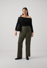 Černý žebrovaný top bez ramínek s volnými zelenými žebrovanými kalhotami. Modelka drží černou tašku a má na sobě černé podpatky.