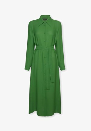 Pitkä vihreä nappilista, leveällä kauluksella, pitkät hihat ja samaa kangasta oleva vyö sidottuna vyötärölle.