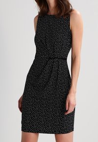 Black sleeveless dress with white polka dots, fitted waist, and knee-length design. Smooth texture and subtle gathering at waist create shape.