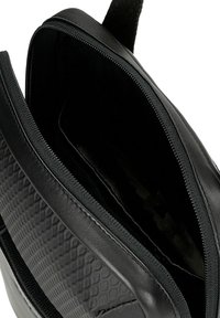 Borsa nera in pelle con un design trapuntato e texture. Dotata di chiusura con zip e un interno spazioso, foderato in un tessuto liscio.
