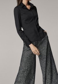Camicia nera a maniche lunghe con colletto, abbinata a pantaloni grigi a gamba larga con un motivo a trama.