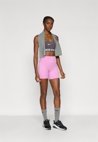 Nike sportski grudnjak u sivoj boji s crnim logotipom, ružičaste kratke hlače, siva marama za vrat, sive čarape i crne tenisice s bijelim detaljima.