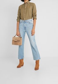 Olivově zelená košile na knoflíky, světle modré džíny rovného střihu, béžová kabelka s třásněmi a hnědé kotníčkové boty. Jednoduchý design s klasickou siluetou.