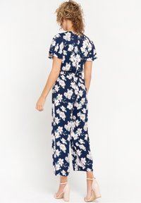 Námořnický květinový overal s krátkými rukávy, se zúženým pasem a širokými nohavicemi, s bílými a růžovými květinovými vzory a měkkou, lehkou tkaninou.