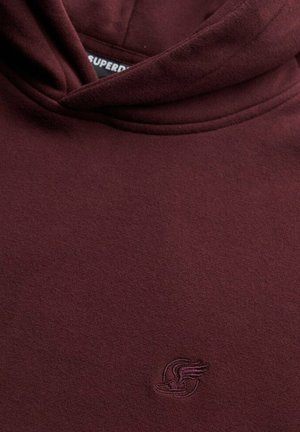 Bordowy bluza z kapturem wykonana z miękkiego materiału, z sznurkiem na kapturze i małym haftowanym logo na klatce piersiowej. Gładka tekstura.