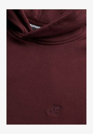 Sudadera color burdeos de tela suave, con capucha ajustable y un pequeño logo bordado en la zona del pecho. Textura lisa.