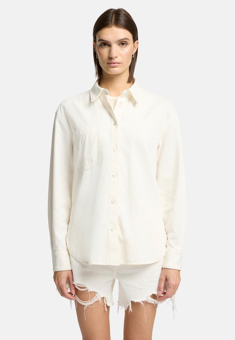 Chemise blanche à boutons, en tissu doux, avec une poche poitrine, un col classique et des manches longues, associée à un short blanc déchiré.