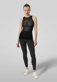 Top senza maniche nero con un intricato motivo in pizzo, abbinato a leggings neri aderenti e sneakers bianche. Tessuto liscio e design aderente.