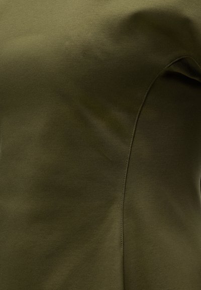 Κοντινό πλάνο υφάσματος ελιάς με ορατή ραφή και λεπτή υφή, που δείχνει μια καμπυλωτή λεπτομέρεια ραφής.