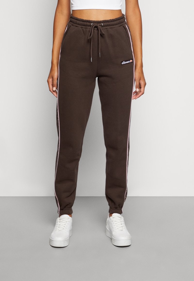 Pantaloni sportivi marroni con strisce laterali bianche e rosa, dotati di una vita elastica e polsini. Abbinati a sneakers con la piattaforma bianche.