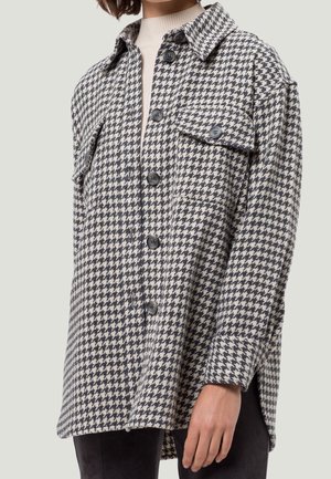 Veste-chemise oversize pour femmes à motifs pied-de-poule avec poches à rabat sur le devant et manches longues, portée sur un pull col roulé beige.