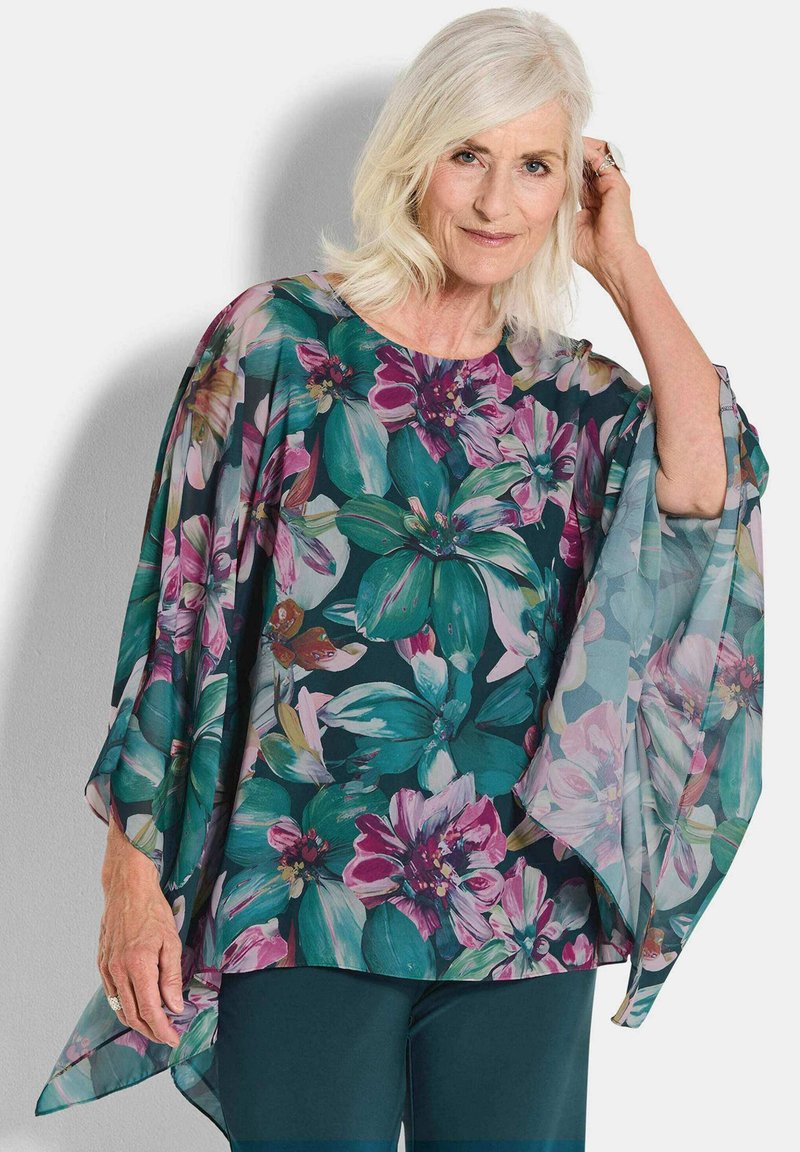 Losse groene bloemen-top met grote roze en paarse bloempatronen. Doorzichtige, lichte stof met brede mouwen en een ronde halslijn.