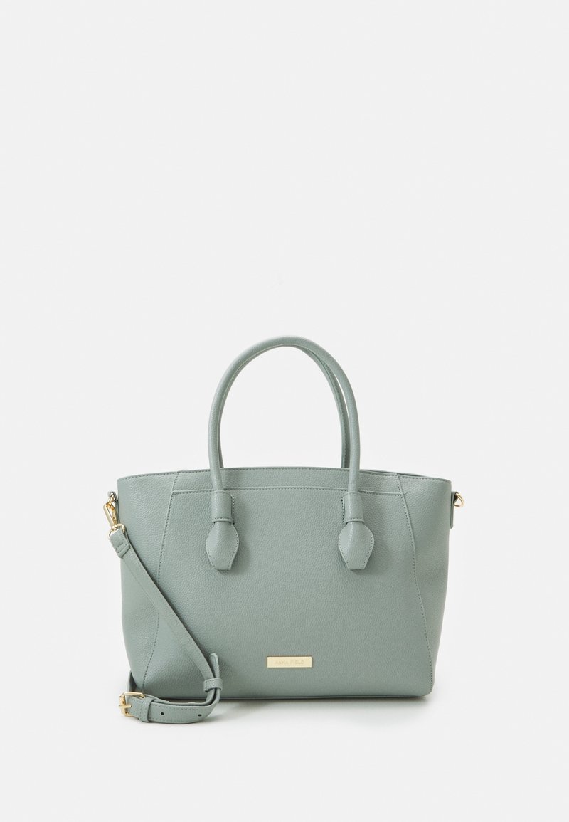 Jasnozielona, strukturalna torebka z ekoskóry z dwoma górnymi uchwytami, regulowanym paskiem na ramię i złotym logo na przedniej stronie.