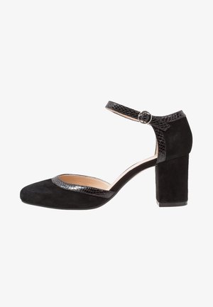 Chaussure à talon haut en daim noir avec un bout carré, une bride de cheville texturée noire et un épais talon bloc. Présente un détail de bride lisse en contraste.