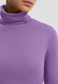 Golf z długim rękawem wykonany z elastycznego fioletowego materiału. Charakteryzuje się dopasowanym krojem i miękką teksturą, z minimalnie widocznymi szwami.