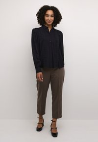 Cămașă albastră cu butoni, cu detalii din dantelă pe față. Mâneci lungi cu manșete, asortată cu pantaloni eleganți maro și pantofi cu toc bloc negri.