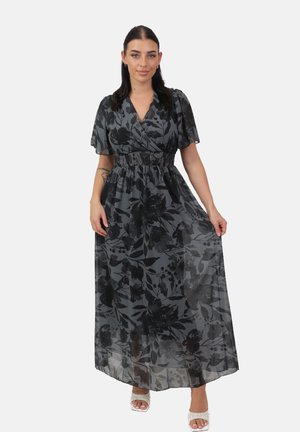 Fließendes, schwarzes Maxikleid mit floralen Mustern, kurzen Ärmeln, V-Ausschnitt, elastischem Bund und transparenter Überlage. Weiße Sandaletten mit Absatz runden den Look ab.