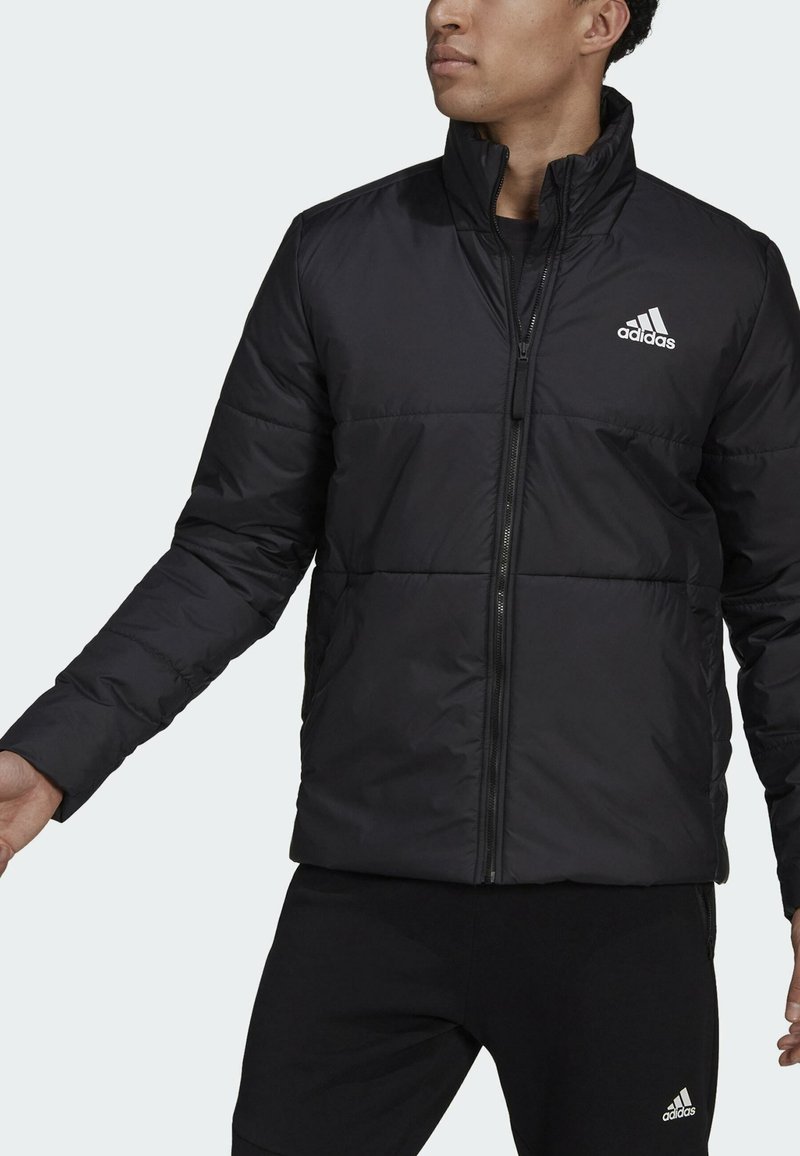 Giacca a vento nera con zip frontale, caratterizzata da un collare alto, pannelli cuciti e un piccolo logo bianco Adidas sul lato sinistro del petto.