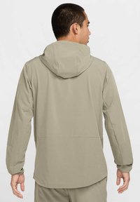 Lichtgewicht grijze jas met capuchon, met een gladde textuur, lange mouwen en een losse pasvorm, ontworpen voor comfort en bewegingsvrijheid.