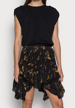 Femme portant un haut noir sans manches et une jupe asymétrique noire avec des motifs floraux jaunes et une bordure en dentelle.