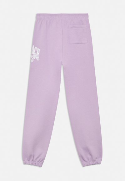 Lila melegítő nadrág elasztikus derékpánttal és mandzsettákkal, egy hátsó zsebbel, és a bal combon részben látható fehér grafikával ellátva.