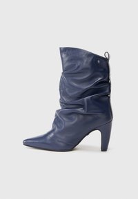 Cizmă din piele de culoare albastru marin, cu vârful ascuțit, design pliat și toc înalt. Prezintă o ușoară strălucire și un manșon de prindere în spate.