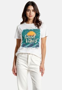 Witte katoenen T-shirt met een groen en blauw grafisch ontwerp met de tekst "Good Vibes," waarop een zon en oceaangolven te zien zijn.