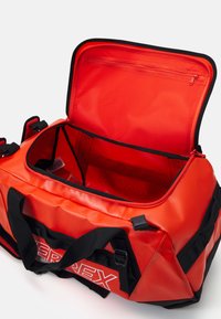 Röd vattentät duffelväska med svarta detaljer, dragkedja upptill, dubbla handtag och en inre dragkedjeficka. Robust tyg, fyrkantig form.